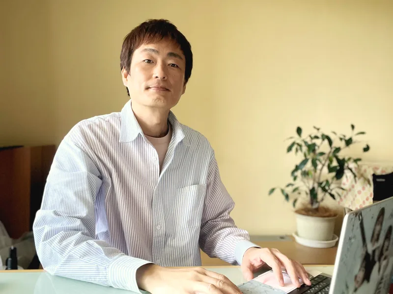 管理人コナン。自宅のデスクでノートPCに向かい、こちらを見ている。